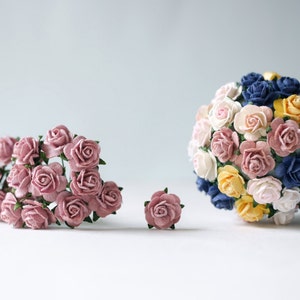 Może przedstawiać: Kolekcja papierowych róż w różnych kolorach, w tym różowym, białym, żółtym, niebieskim i granatowym. Róże są ułożone w bukiet i mniejszą grupę.