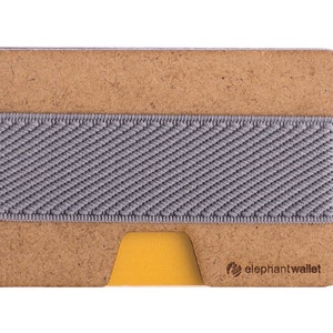 May include: A brown leather wallet with a gray elastic band and a yellow card slot. The wallet has the text "elephantwallet" printed on the bottom right corner.