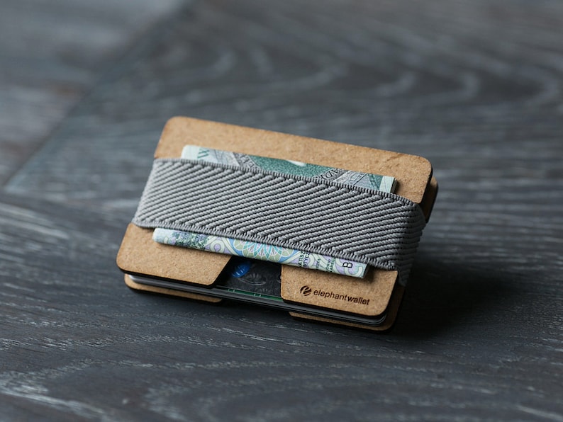 May include: A wooden wallet with a gray elastic band and the text "elephantwallet" printed on the front. The wallet is open and contains a few bills.