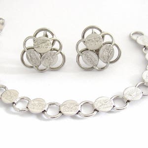 Puede incluir: Un collar de cadena de plata con un colgante de plata con un diseño circular con cinco círculos entrelazados. El colgante está hecho de varios círculos pequeños que están conectados entre sí para formar un círculo más grande.