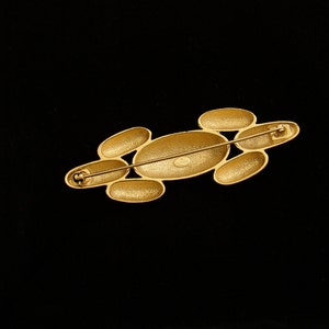 May include: Gold-toned brooch with a cluster of oval-shaped stones. The brooch has a pin and catch closure.