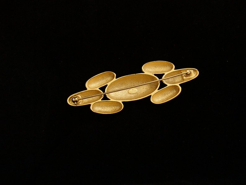 May include: Gold-toned brooch with a cluster of oval-shaped stones. The brooch has a pin and catch closure.