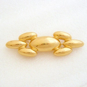 May include: A gold-toned brooch made of multiple oval-shaped pieces. The brooch is a cluster of smooth, rounded, connected ovals.