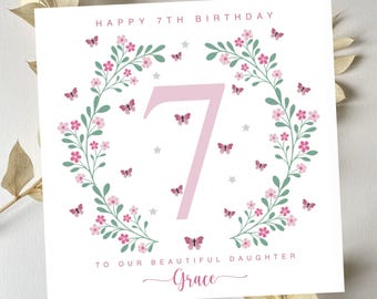 May include: A white card with a pink floral wreath and butterflies surrounding the number 7. The text "Happy 7th Birthday" is at the top of the card and "To our beautiful daughter Grace" is at the bottom.