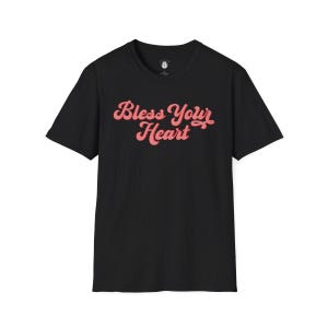 Puede incluir: Camiseta negra con un gr&aacute;fico rojo "Bless Your Heart" en una fuente retro.