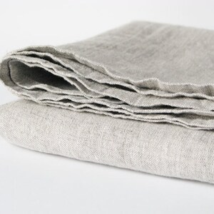 May include: A folded linen throw blanket in a light gray color. The blanket is made of natural fibers and has a soft, textured surface.