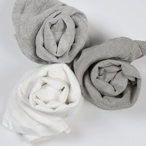 May include: Three fabric cloths rolled up into a rose shape. One cloth is white, and the other two are gray.