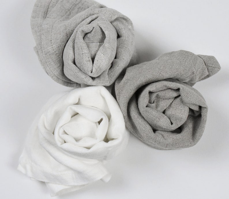 May include: Three fabric cloths rolled up into a rose shape. One cloth is white, and the other two are gray.