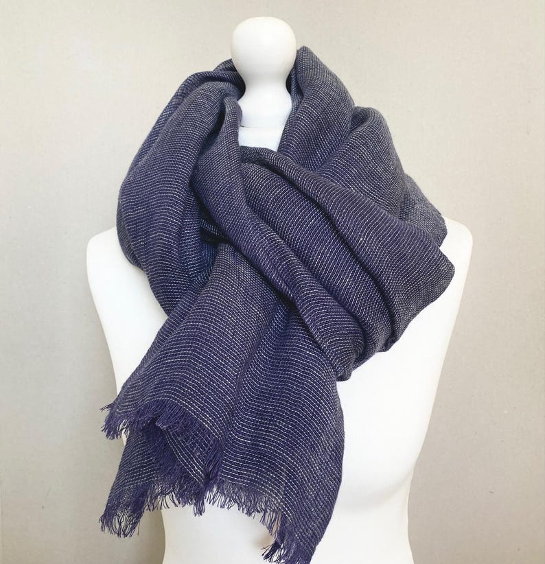 May include: A navy blue scarf with a subtle white stripe pattern and fringed edges. The scarf is draped over a white mannequin, showcasing its texture and drape. The scarf appears soft and lightweight, suitable for cooler weather.
