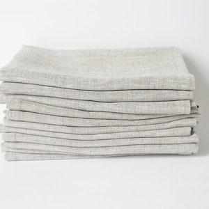 May include: A stack of 12 linen napkins in a light gray color. The napkins are folded and stacked neatly.