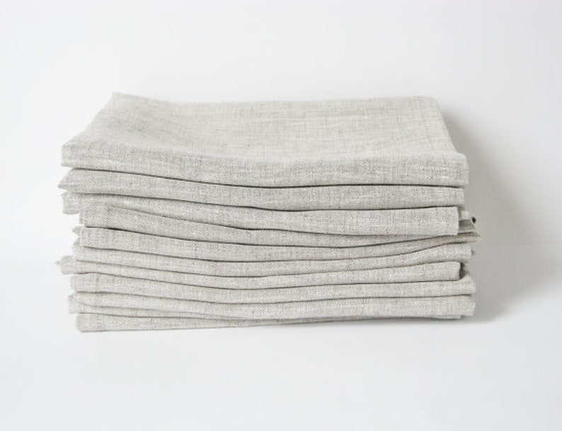 May include: A stack of 12 linen napkins in a light gray color. The napkins are folded and stacked neatly.
