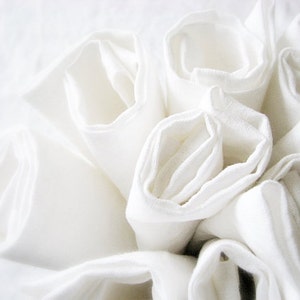 May include: A close-up of a stack of white fabric napkins, rolled and arranged in a circular pattern.