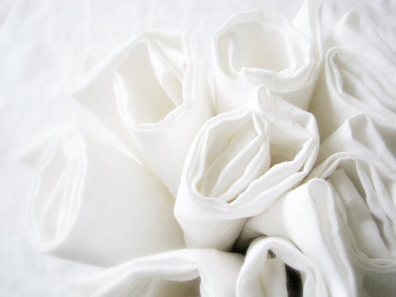 May include: A close-up of a stack of white fabric napkins, rolled and arranged in a circular pattern.