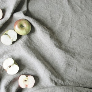 May include: Four halved apples on a gray linen background. Two apples are green and two are red.