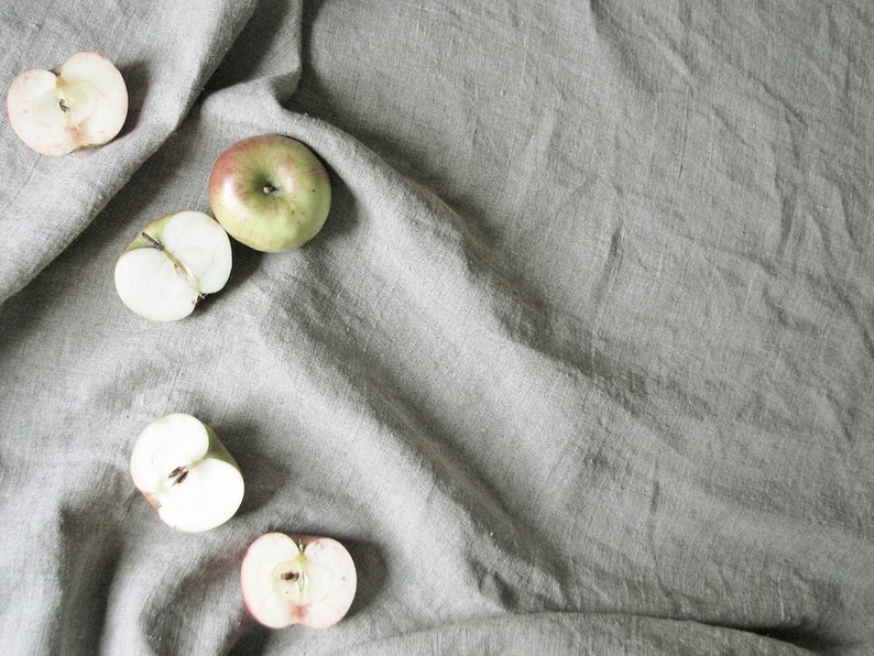 May include: Four halved apples on a gray linen background. Two apples are green and two are red.