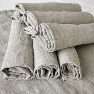 May include: A stack of six rolled linen napkins in a light beige color. The napkins are folded and rolled neatly, creating a uniform and elegant appearance.