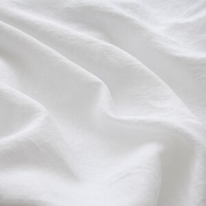 May include: White fabric with soft wrinkles and folds. The fabric is smooth and has a subtle texture.