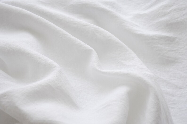 May include: White fabric with soft wrinkles and folds. The fabric is smooth and has a subtle texture.