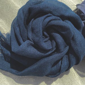 May include: A close-up of a navy blue scarf, artfully arranged in a spiral. The fabric has a soft texture and a fringed edge. Another scarf is partially visible on the right. The scarves are likely made of a lightweight material, perfect for adding a touch of elegance.