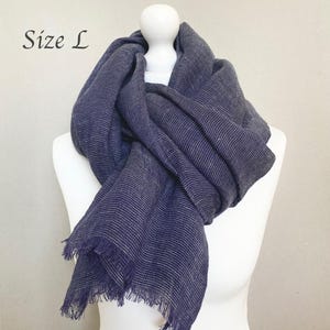 May include: A navy blue scarf with white stripes and fringed edges is draped over a white mannequin. The text "Size L" is in the upper left corner. The scarf is made of a soft, woven material.