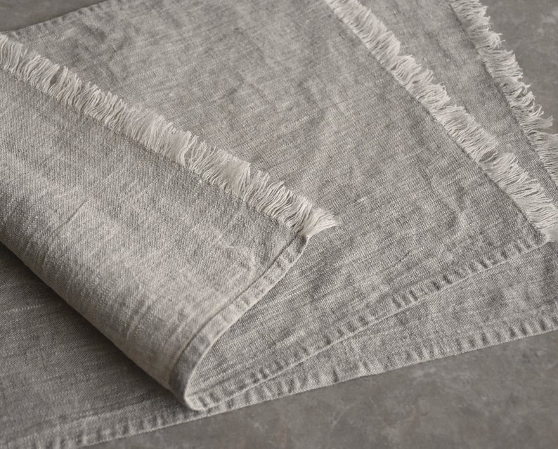 May include: A gray linen table runner with a frayed edge. The runner is folded in half and has a soft, textured surface.