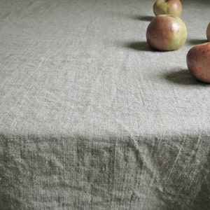 May include: A close-up of a gray linen tablecloth with four red apples on it.