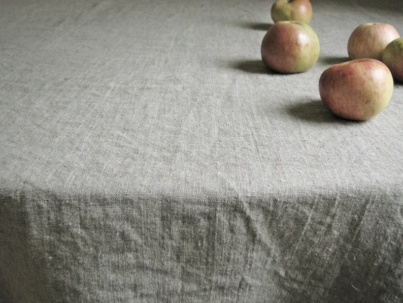 May include: A close-up of a gray linen tablecloth with four red apples on it.