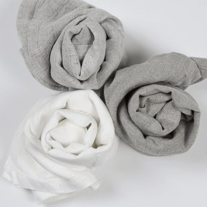 May include: Three fabric cloths rolled up into a rose shape. One cloth is white, and the other two are gray.