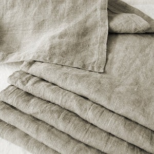 May include: A stack of six linen napkins in a light beige color. The napkins are folded and arranged neatly.