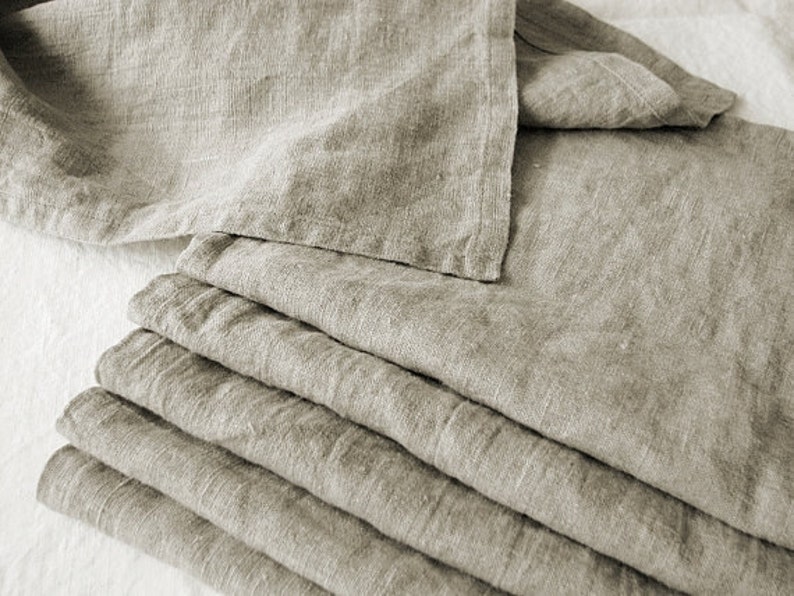 May include: A stack of six linen napkins in a light beige color. The napkins are folded and arranged neatly.