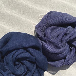 May include: Two navy blue scarves are artfully arranged, showcasing their soft texture. The scarves are made of a lightweight fabric, with a subtle sheen. The fabric is tightly woven, and the scarves are perfect for adding a touch of elegance to any outfit.