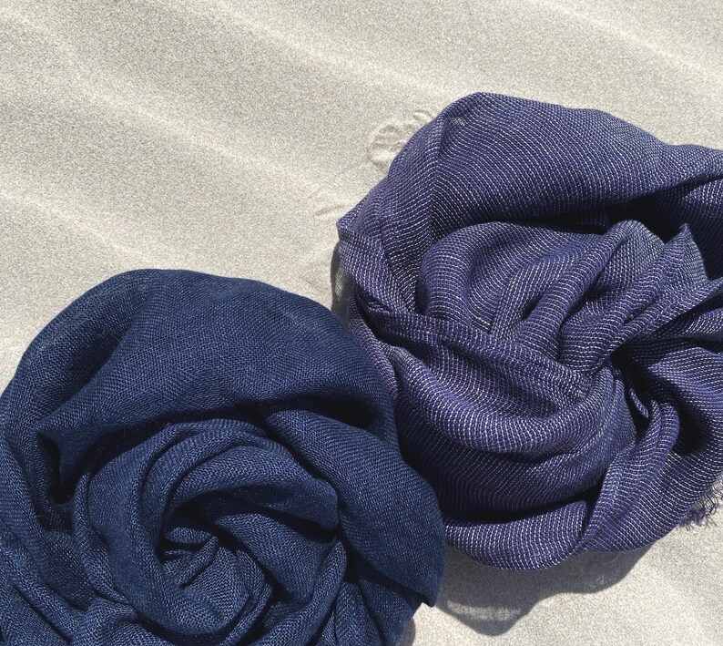 May include: Two navy blue scarves are artfully arranged, showcasing their soft texture. The scarves are made of a lightweight fabric, with a subtle sheen. The fabric is tightly woven, and the scarves are perfect for adding a touch of elegance to any outfit.