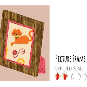 May include: A brown wooden picture frame with a pink and white patterned mat. The frame is tilted and has a cat with a red collar and a ball of yarn inside the frame.