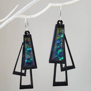 May include: A pair of black geometric earrings with iridescent green and blue glitter embedded in the center of each earring.