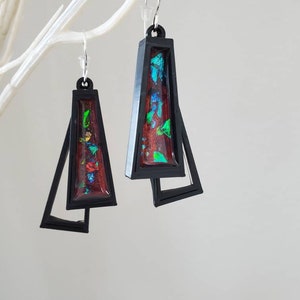 May include: A pair of black geometric earrings with red, green, and blue iridescent resin inserts.