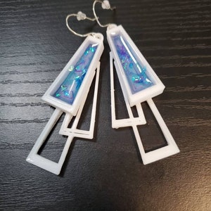 May include: White geometric earrings with blue glitter embedded in the center of each earring.