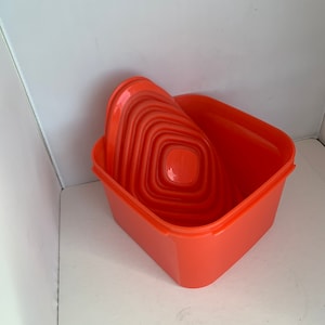 May include: A set of orange plastic nesting containers with a square base and a rounded lid. The containers are stacked inside each other.