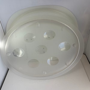 May include: A clear plastic round cake stand with a raised edge and a center circle with six smaller circles. The stand has the word "Tupperware" printed on the side.