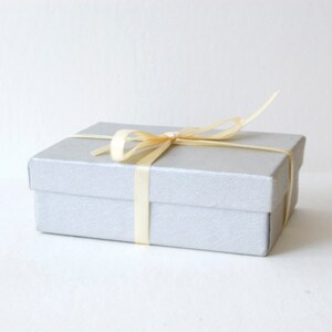 May include: A silver gift box with a cream-colored satin ribbon tied in a bow.