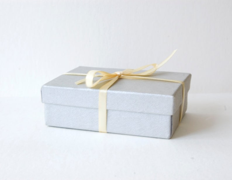 May include: A silver gift box with a cream-colored satin ribbon tied in a bow.