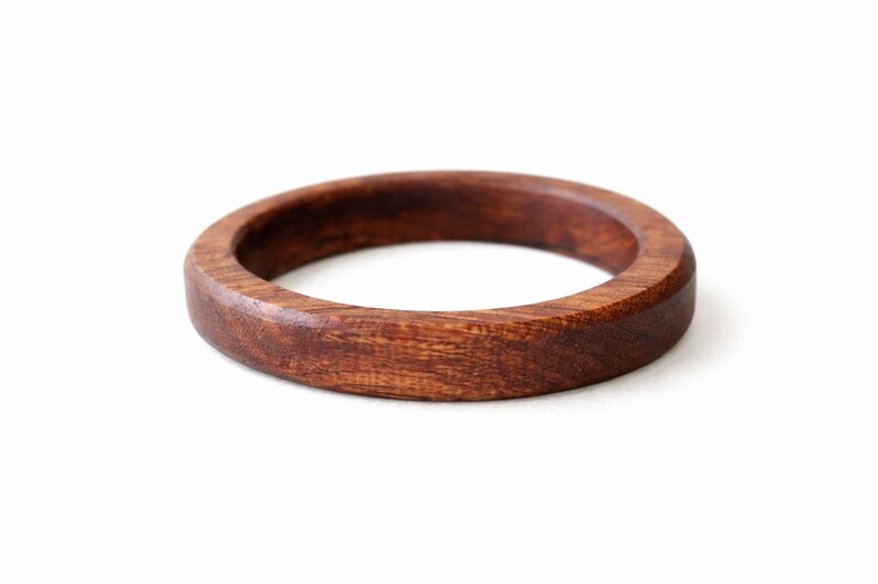 May include: A round, wooden bracelet with a rich, dark brown color. The bracelet is made of a solid piece of wood and has a smooth, polished finish. The bracelet is approximately 2.5 inches in diameter and 0.75 inches wide.