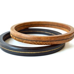 May include: Two wooden bangles, one black and one brown, with a thin gold line around the edge of each.