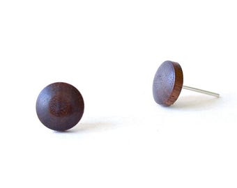 May include: A pair of circular stud earrings featuring a dark brown wood grain finish. Each earring has a smooth, rounded surface and a silver-toned metal post extending from the back, designed for secure attachment to the earlobe.
