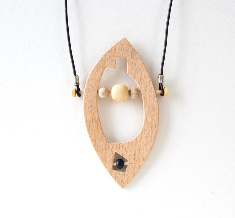 May include: A wooden pendant necklace with a leaf-shaped design. The pendant has a cutout in the shape of a heart and features a black bead and wooden beads.