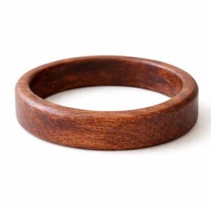 May include: A round, wooden bracelet with a rich, dark brown color. The bracelet is made of a solid piece of wood and has a smooth, polished finish. The design is simple and classic, suitable for everyday wear. The bracelet's diameter is approximately 3 inches.