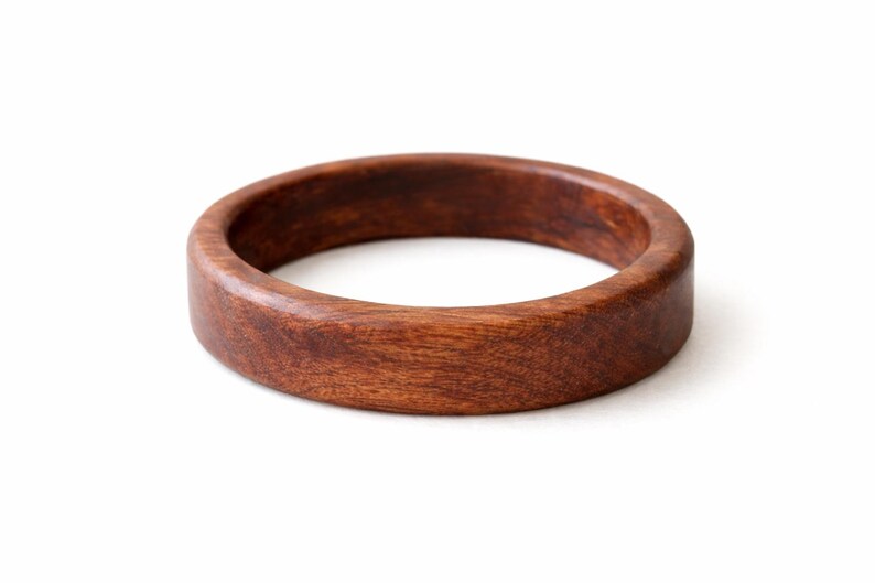 May include: A round, wooden bracelet with a rich, dark brown color. The bracelet is made of a solid piece of wood and has a smooth, polished finish. The design is simple and classic, suitable for everyday wear. The bracelet's diameter is approximately 3 inches.