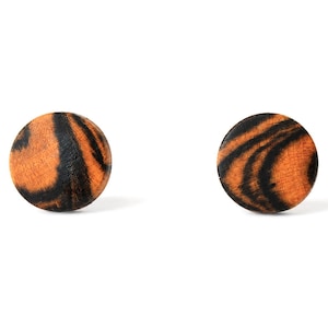 May include: A pair of circular stud earrings featuring a natural wood grain pattern with contrasting orange and black swirls. The round wooden surfaces are polished and display a distinct organic texture with dark streaks across the surface.