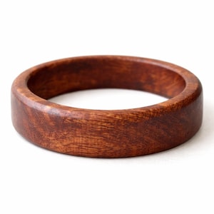 May include: A handcrafted wooden ring with a rich, reddish-brown hue. The ring is made of solid wood and has a smooth, polished finish. The ring is approximately 1 inch wide and is a simple, elegant piece of jewelry.