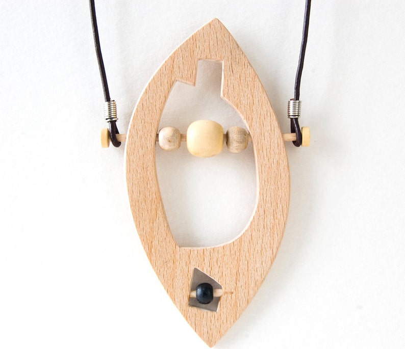 May include: A wooden pendant necklace with a leaf-shaped design. The pendant has a cutout in the shape of a bottle and features wooden beads and a black bead.