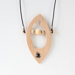 May include: A wooden pendant necklace with a unique shape and a black bead. The pendant is strung with wooden beads and hangs from a black cord.